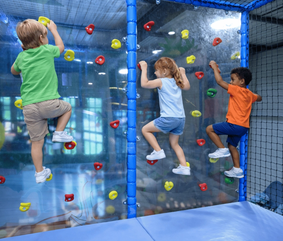 Enfants grimpant un mur d'escalade dans un parc de jeux couvert