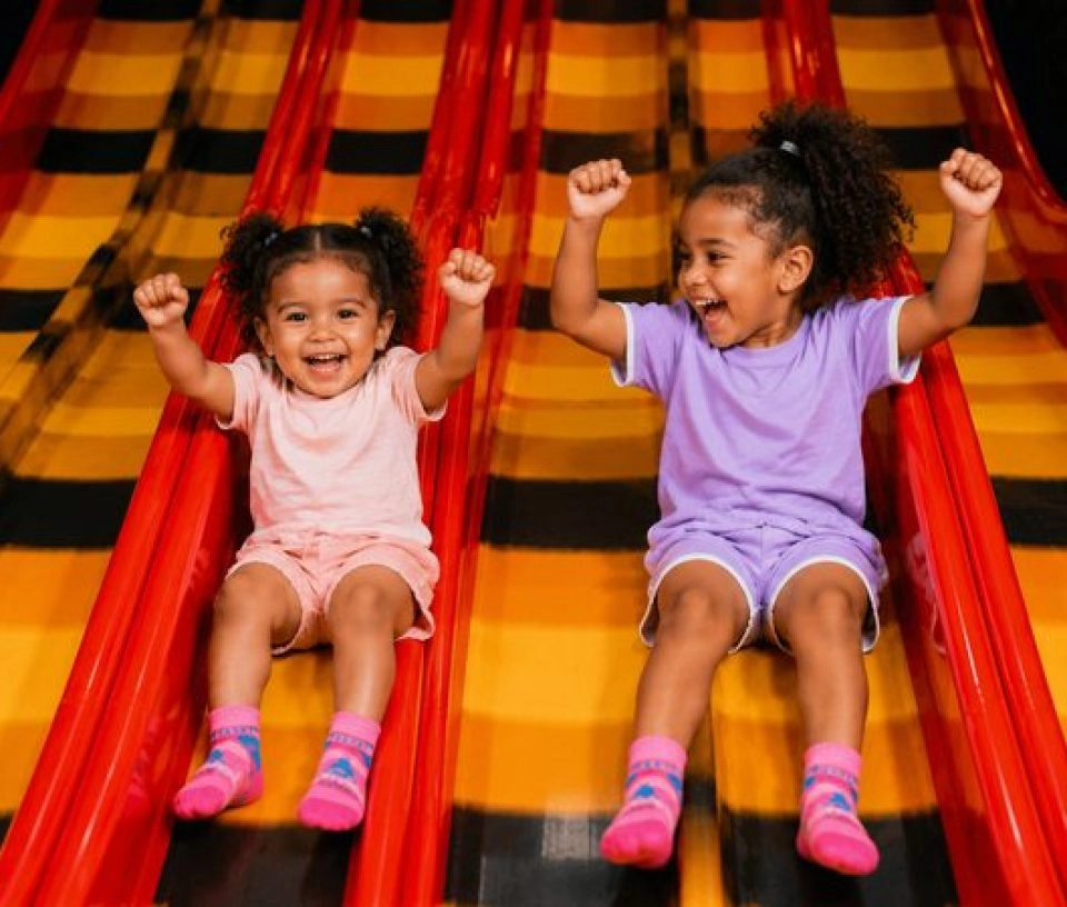 Deux enfants souriants descendant d'un toboggan dans une aire de jeux pour enfants